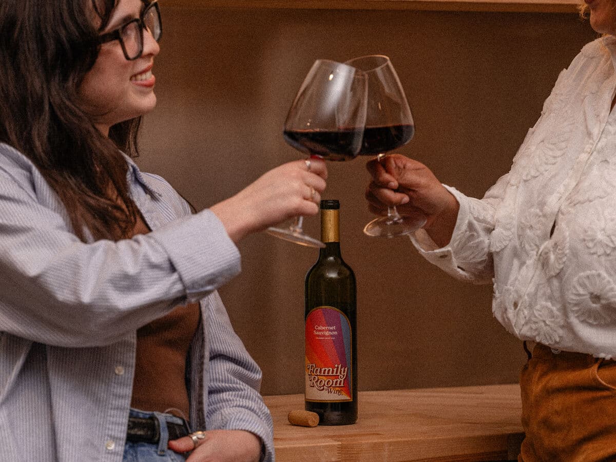 Two friends clinking glasses of Family Room Cabernet Sauvignon in a kitchen
