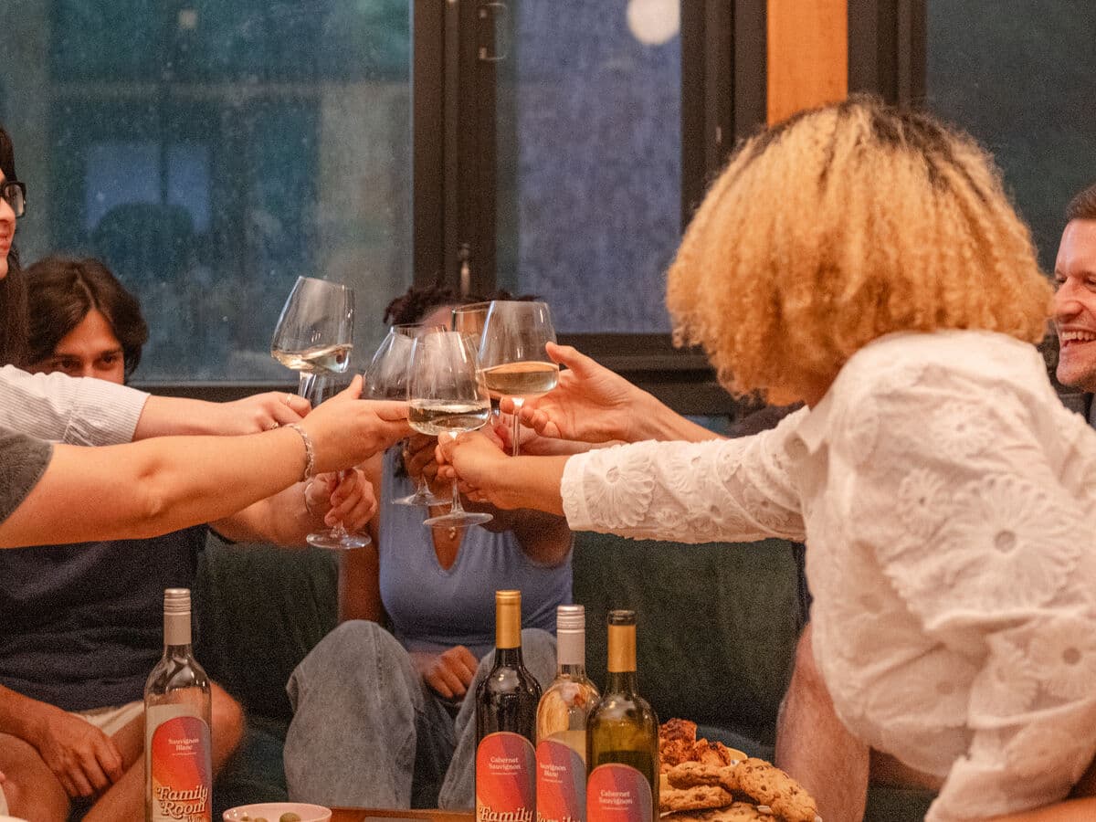 Friends on a couch raising their glasses over Family Room bottles
