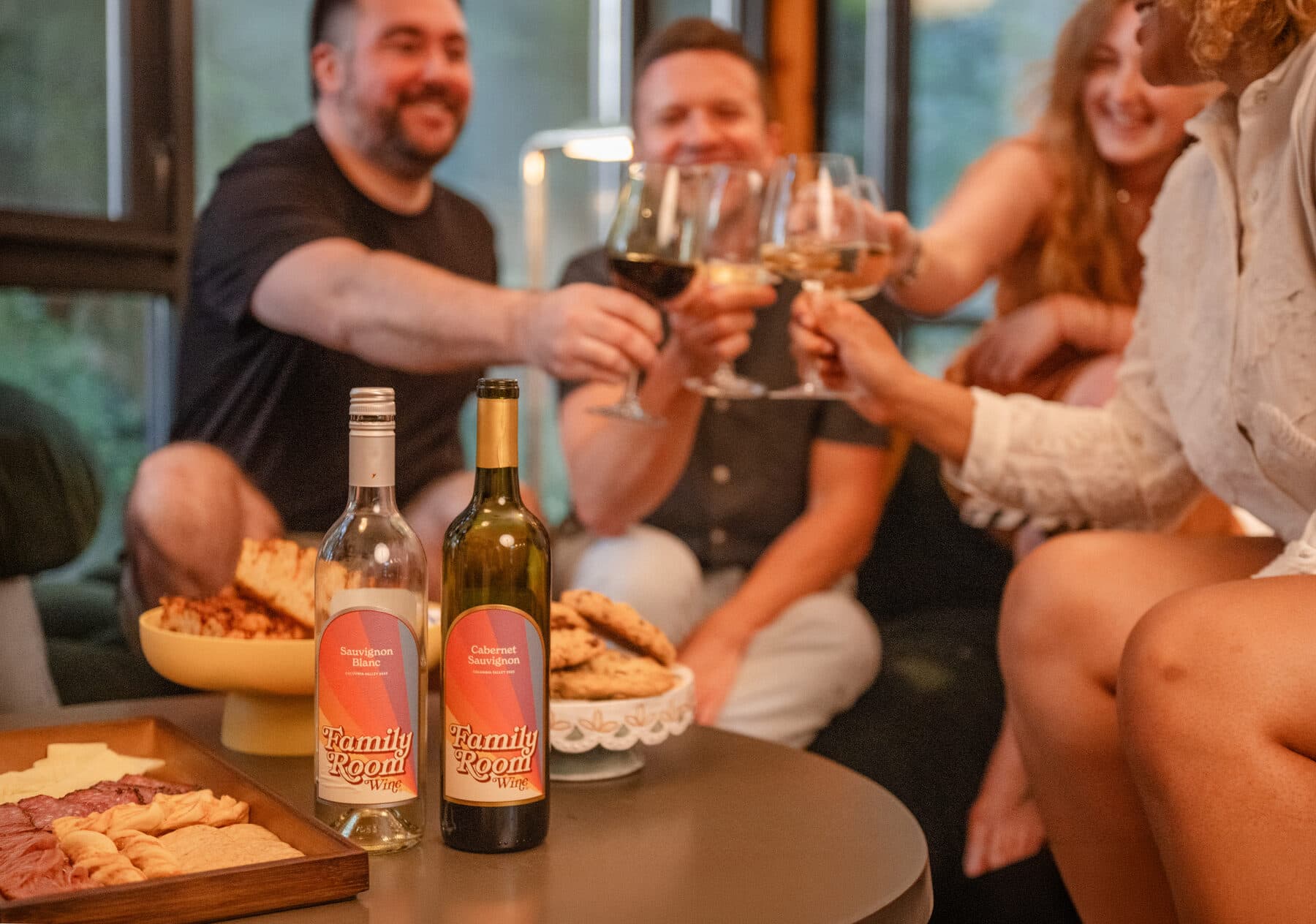 Friends toasting on the couch with Family Room Cabernet Sauvignon and Sauvignon Blanc on the table